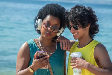 Telefonlarında müzik çalarken sahilde içki içen çift.