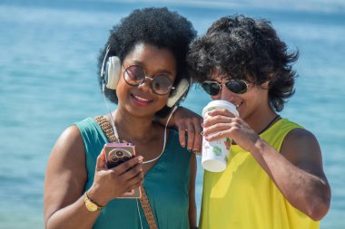 Telefonlarında müzik çalarken sahilde içki içen çift.