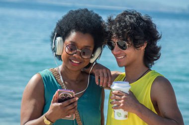 Çift plajda kulaklık ve cep telefonuyla eğleniyor.