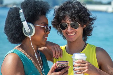 Çift plajda kulaklık ve cep telefonuyla eğleniyor.