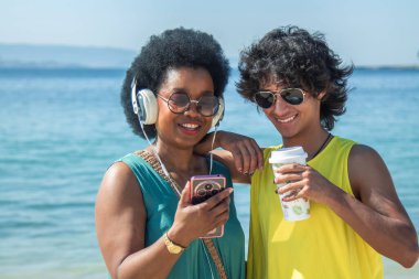 Çift plajda kulaklık ve cep telefonuyla eğleniyor.