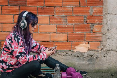 Spor kıyafetli genç bir kadın telefonunu sokakta kullanıyor.