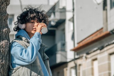 Latin kökenli genç bir adam kulaklık takıyor ve içki içiyor.