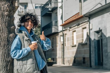 Kulaklıklı ve paket servisi yapan genç adam parmaklarıyla iyi bir hareket yapıyor.