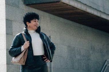 Deri giymiş orta yaşlı bir kadın şehirde yürüyor.