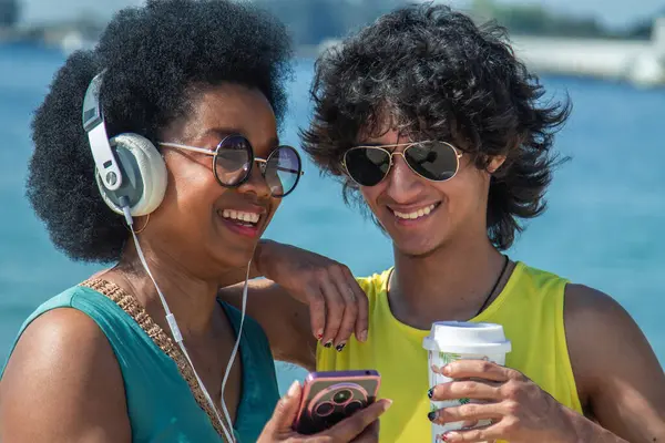 Çift plajda kulaklık ve cep telefonuyla eğleniyor.