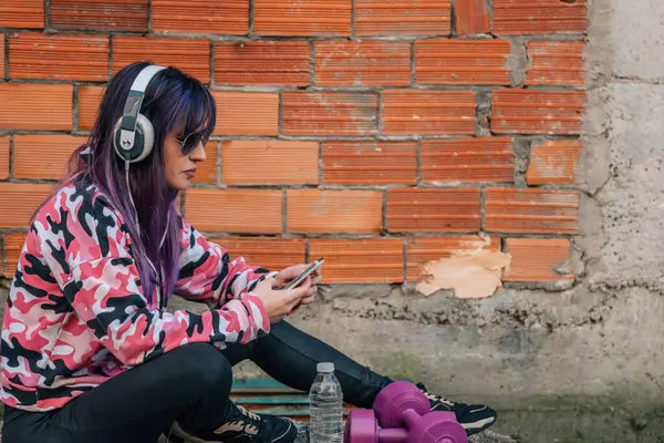 Spor kıyafetli genç bir kadın telefonunu sokakta kullanıyor.