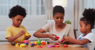 Annesi evde oyuncaklarla oynayan Afrikalı Amerikalı çocuklar.