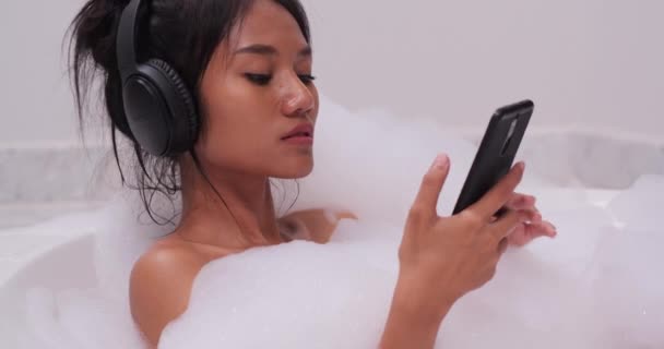 一个女孩洗澡和在智能手机上听音乐的镜头 — 图库视频影像