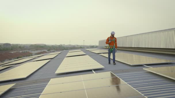 ソーラーパネル付きの建物の屋根の上を歩くハードハットの男性労働者 — ストック動画