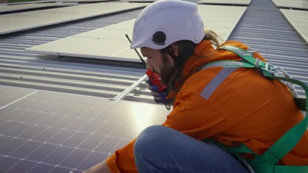 ソーラーパネル付きの建物の屋根の上でウォーキートーキーとハードハットの男性労働者 — ストック動画