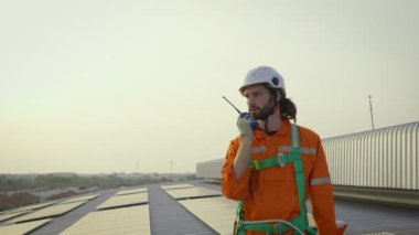 Binanın çatısında güneş panelli telsizli kasketli bir erkek işçi. 