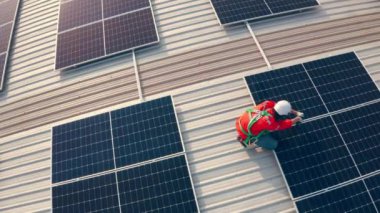 Binanın çatısına güneş panelleri kuran kasklı bir erkek işçi.