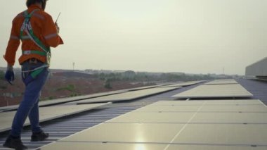 Binanın çatısında güneş panelleriyle yürüyen kasklı bir erkek işçi.