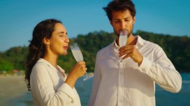 Mutlu ve neşeli bir çift sahilde şampanya içiyor.