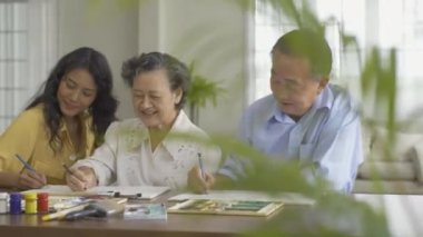 Torunlarıyla birlikte evde resim çizen kıdemli bir adam ve kadın.