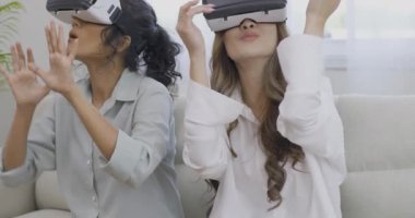 Oturma odasında sanal gerçeklik kulaklığı kullanan iki genç kadın.
