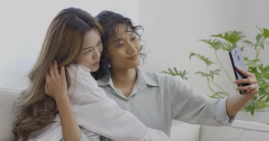 Oturma odasındaki kanepede otururken selfie çeken genç kadınlar.