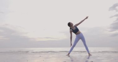 Genç kadın plajda yoga yapıyor.