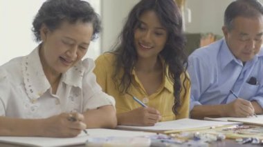 Torunlarıyla birlikte evde resim çizen kıdemli bir adam ve kadın.