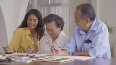 Torunlarıyla birlikte evde resim çizen kıdemli bir adam ve kadın.