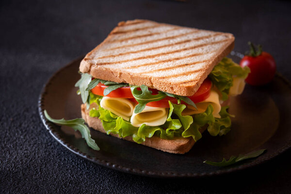 Вкусный сэндвич с поджаренным хлебом, салатом, сыром и помидорами.