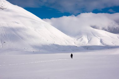 Kış manzarası, tepelerin arasında kar vadisinde yürüyen adam.