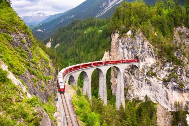 İsviçre kırmızı treni dağda viyadük üzerinden geçiyor, manzaralı bir yolculuk