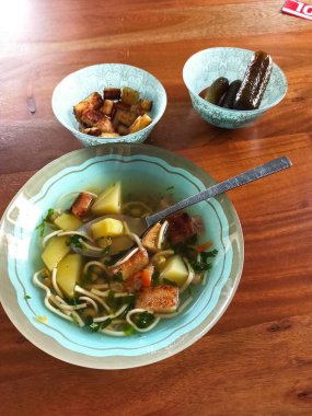 Ev yapımı sıcak şehriye çorbası turşu ve ahşap masada kızarmış patatesle servis edilir..