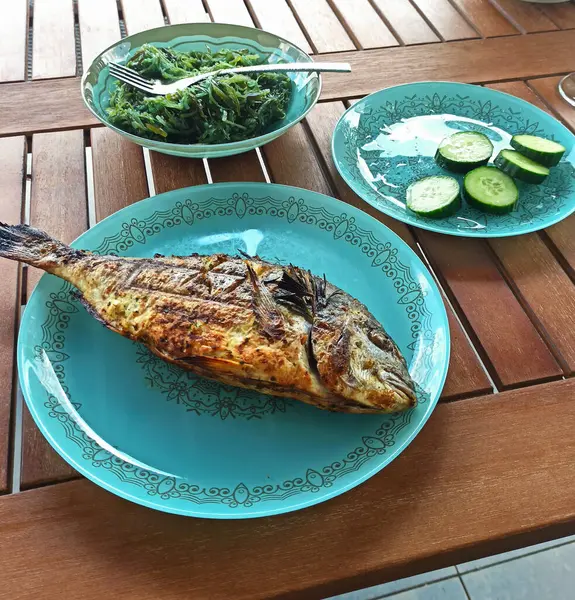 kavrulmuş dorado veya limon ve portakal dilimleri ile çipura balık, baharatlar, taze maydanoz ve ıspanak arka plan üzerinde malzemeler ile eski ahşap masada beyaz tabak, yukarıdan yatay görünümü.