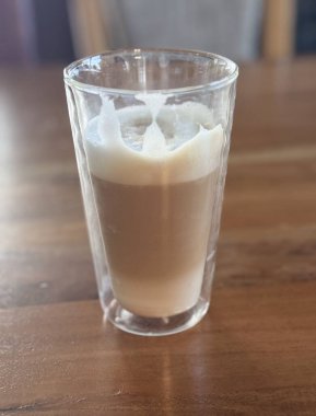 Dalgona kahveli büyük şeffaf kupa. Soğuk sütün içinde güzelce ve güzelce çırpılmış kahve köpüğü serpiştirilmiş. Dalgona, kahve çekirdekleri, süt şişesi, şeker kasesi ve tarçın çubukları.