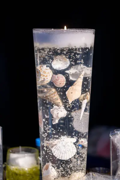 Transparent burning candle with shells and snails incorporated in the transparent candle wax with a very nautical flair