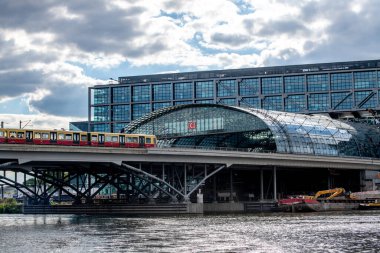 Berlin, Berlin / Almanya - 09 03 2022: S-Bahn 'ın Spree Nehri üzerindeki bir köprünün üzerinden geçmekte olduğu Berlin' deki ana istasyon. İstasyonun ön cephesinde sonsuz cam levhalar var.