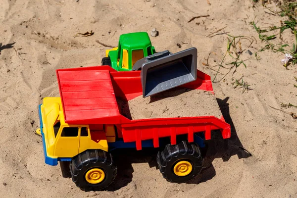 A small plastic toy truck that is loaded with sand by a toy wheel loader. The truck is a tipper that is used to transport sand