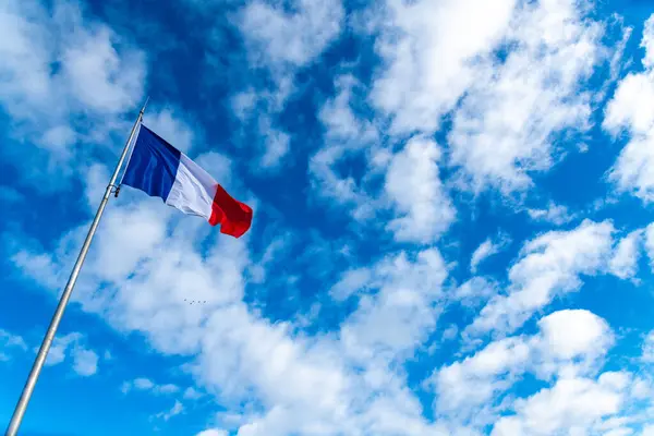 The French flag in the wind in front of a blue sky with veil clouds and a beautiful light. The flag is positioned in time on the photo with plenty of space for text