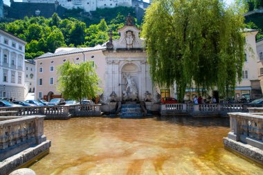 Salzburg, Salzburg - Avusturya 06-17-2021: Kapitelschwemme veya At Kuyusu, Salzburg 'da ortasında bina ve ağaçlarla çevrili bir çeşme.