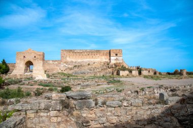 Sagunt, Valencia - İspanya - 09-07-2021: Sagunt 'taki kale manzarası, kalın duvarlar, büyük bir kapı, kısmen harap olmuş binalar ve temeller, hepsi mavi gökyüzünün altında.