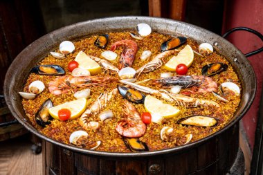 Kahverengi pirinç, limon, deniz ürünleri ve küçük domatesli büyük bir paella tavası. Karides, midye ve midye kabukları görebilirsiniz. Tava çok kullanılmış görünüyor..