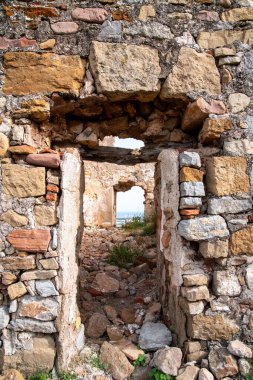 Kaba taştan yapılmış eski, harap bir bina. Manzara önce girişten, sonra pencereden geçiyor..
