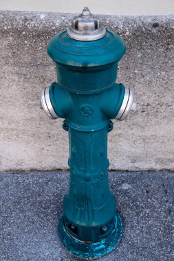 İki tıkırtı noktası olan yeşil bir yangın musluğu ve düzleştirilmiş bir alanda bir ev duvarının önünde bir musluk..