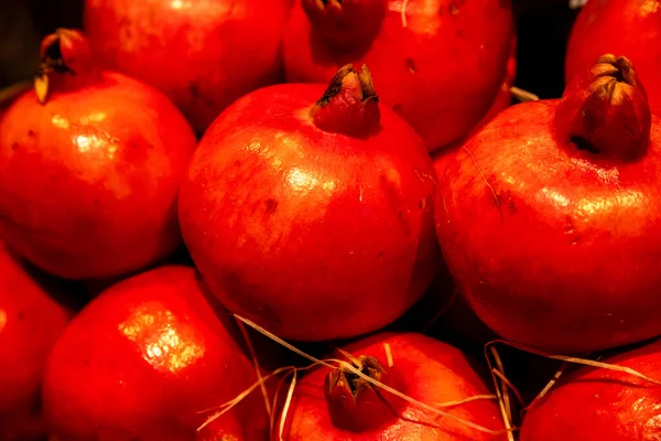 Several freshly harvested red pomegranates in a pile. You can still see the straw that was picked up during the harvest. The light shines on the fruit.