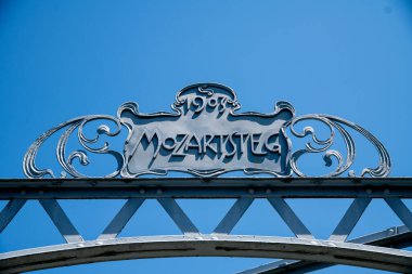 Alman harfleriyle Mozartsteg işareti: Mozartsteg. Metalden yapılmış, yardım mektupları ve mavi gökyüzüne karşı 1903 yılı.