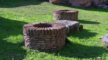 om-Latium - İtalya - 11-23-2022: Roma 'daki Roma Forumu' nun yeşil çimenliğindeki iki tarihi tuğla çeşmesi.