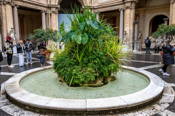 Citta del Vaticano, Vaticano - Stato della Citta del Vaticano - 11-22-2022: Vatikan Müzesi avlusunda tarihi heykel ve ziyaretçilerle çevrili sakin bir fıskiye bulunuyor