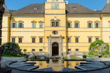 Salzburg, Salzburg - Avusturya - 06-18-2021: Hellbrunn Sarayı 'nın Salzburg' daki sarı cephe ve taş çeşmesinin güneşli manzarası