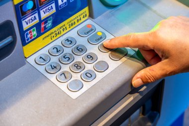 Denia, Alicante - İspanya - 12-22-2023: ATM tuş takımındaki bir düğmeye basarak üzerinde kart logoları bulunan bir parmağın yakın çekimi