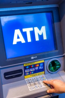 Denia, Alicante - İspanya - 12-22-2023: Büyük 'ATM' metni gösteren mavi ekranlı bir ATM kullanan kişi