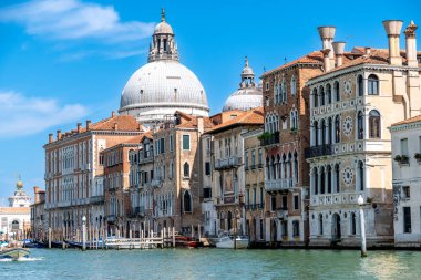 Venice, Veneto - Italy - 06-10-2021: Classic Venetian architecture lines the Grand Canal under a bright blue sky with Basilica di Santa Maria della Salute in the background clipart