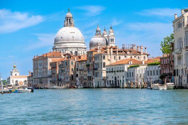 Venice, Veneto - Italy - 06-10-2021: Classic Venetian architecture lines the Grand Canal under a bright blue sky with Basilica di Santa Maria della Salute in the background clipart