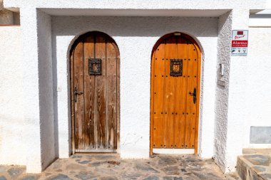 Puerto de Mazarron, Murcia - İspanya - 01-18-2024: Kemerli beyaz cephedeki ahşap kapılar, farklı koruma alanlarında demirle süslenmiş